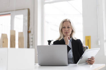 Unternehmerin mit Laptop und digitalem Tablet auf dem Schreibtisch im Heimbüro - MOEF03230