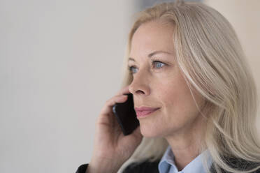 Nahaufnahme eines weiblichen Berufstätigen, der mit einem Mobiltelefon an der Wand eines Büros spricht - MOEF03237