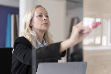 Unternehmerin schreibt mit Filzstift am Fenster im Home Office - MOEF03240