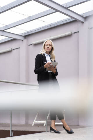 Geschäftsfrau mit digitalem Tablet an einem Geländer im Büro stehend, lizenzfreies Stockfoto