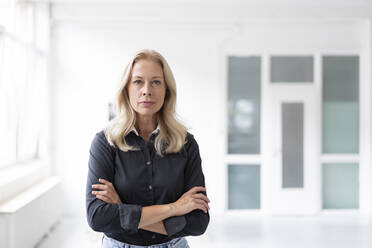 Confident female professional with arms crossed standing in home office - MOEF03256