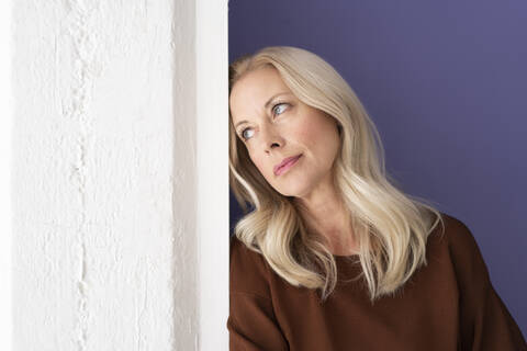 Thoughtful businesswoman looking away while leaning on wall in office stock photo