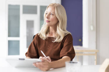 Thoughtful female professional with digital tablet on desk sitting at home - MOEF03270