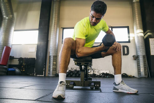 Male athlete lifting dumbbell while sitting in gym - ABZF03277