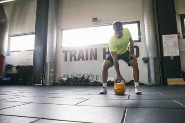 Männlicher Sportler hebt eine Kettlebell, während er im Fitnessstudio auf dem Boden steht - ABZF03282