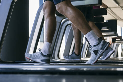 Legs of athletes running on treadmills in health club - ABZF03285