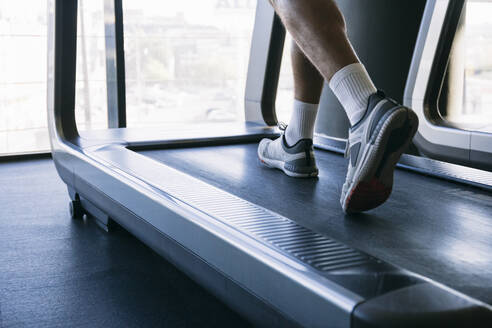 Beine eines männlichen Sportlers, der auf dem Laufband im Fitnessstudio läuft - ABZF03286