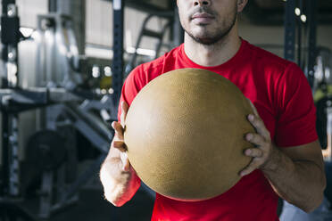 Nahaufnahme eines männlichen Sportlers mit rotem T-Shirt, der einen Sportball in einer Turnhalle hält - ABZF03290