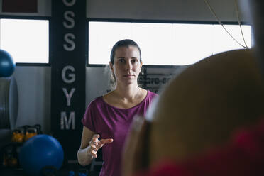 Fitness-Instruktor wirft Ball in Richtung Frau, während er mit ihr im Fitnessstudio trainiert - ABZF03291