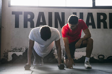 Fitness instructor guiding male athlete exercising with dumbbells on floor in gym - ABZF03292