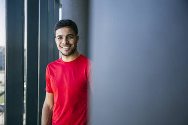 Smiling male athlete wearing red t-shirt standing in health club - ABZF03299