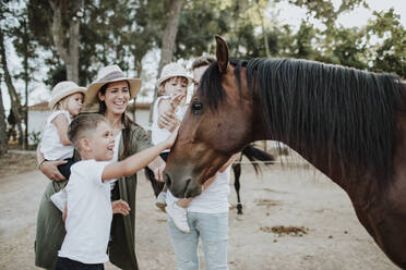 Fröhliche Eltern mit Kindern, die ein Pferd berühren, während sie im Freien stehen - GMLF00567