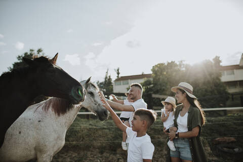 Familie berührt Pferde und steht gegen den Himmel, lizenzfreies Stockfoto