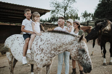 Eltern und Mädchen schauen auf Kinder, die auf einem Pferd sitzen - GMLF00581