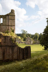 Historisches Steingebäude mit gewölbten Passagen und grünem Gras auf bewölktem Himmel Hintergrund in Abadia de Fountains - ADSF15157