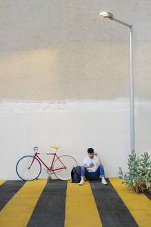 Vorderansicht eines auf dem Boden sitzenden Mannes mit einem Fixie-Fahrrad - ADSF15176