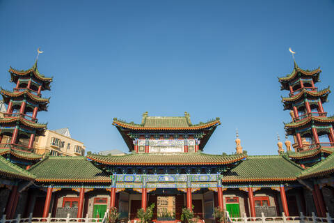 Low angle of exterior of oriental building with curved roof and ornamental pagodas on background of cloudless sky stock photo