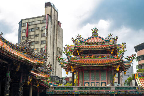 Niedriger Winkel der traditionellen Bangka Lungshan Tempel mit ornamentalen Design in der Nähe der modernen Stadt Gebäude gegen bewölkten Himmel in Taiwan - ADSF15213