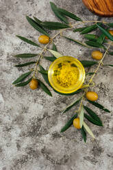 From above top view of glass jar with organic olive oil placed on shabby gray table near fresh green olives and tree branches - ADSF15223