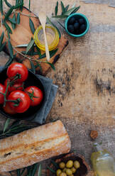 Top view composition of fresh homemade bread loaf placed on wooden table near ripe red tomatoes with green and black olives and olive oil - ADSF15224