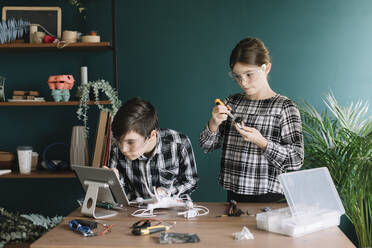 Siblings using digital tablet while preparing drone on table against wall at home - ALBF01517