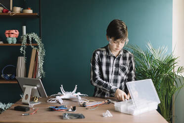 Boy making quadcopter on table while standing against wall at home - ALBF01528