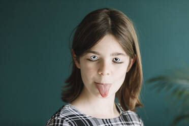 Nahaufnahme eines Mädchens mit Kulleraugen und Make-up, das seine Zunge gegen die Wand zu Hause streckt - ALBF01544