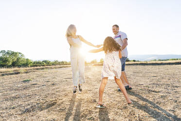 Cheerful parents playing with daughter on land against clear sky during sunny day - JCMF01354