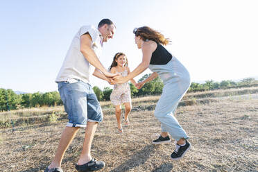 Cheerful parents playing with daughter on land against clear sky - JCMF01355