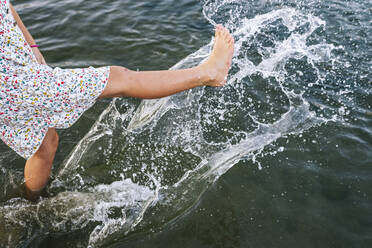 Girl splashing water with legs in lake - JCMF01359