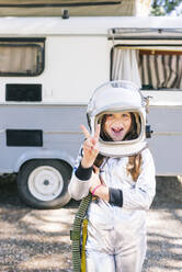 Girl wearing space suit showing peace sign while standing against motor home - JCMF01364