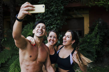 Hemdloser Mann, der ein Selfie mit seinen Freundinnen macht, während er im Hof steht - EBBF00715