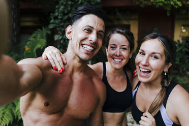 Close-up of shirtless man with cheerful female friends standing in yard - EBBF00717