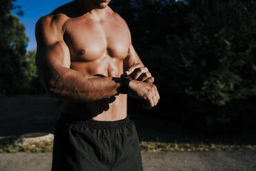 Shirtless male athlete checking time while standing in park - EBBF00723