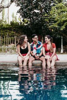 Lächelnde Freunde, die am Pool sitzen und sich unterhalten - EBBF00735