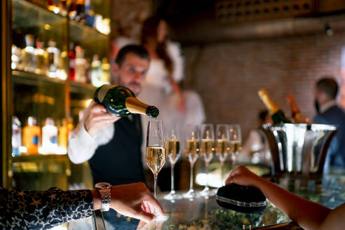 Bartender serving drink to man and woman at bar counter in pub - OCMF01656