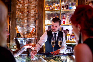 Bartender serving drink to women at bar counter in pub - OCMF01657
