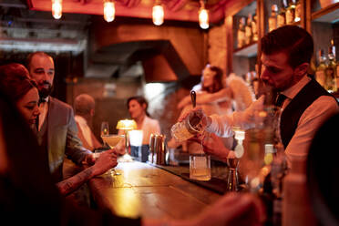 Bartender serving drink while standing at bar counter in pub - OCMF01661