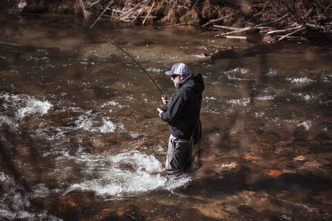 Fly fisherman casting in rapid flowing river at forest stock photo