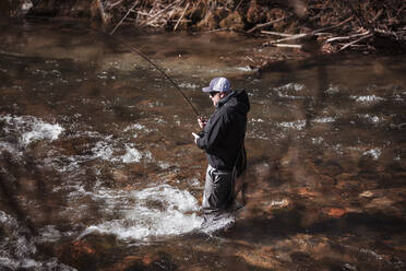 Fly fisherman casting in rapid flowing river at forest - DHEF00378