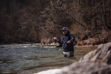 Fisherman casting in flowing river at forest - DHEF00380