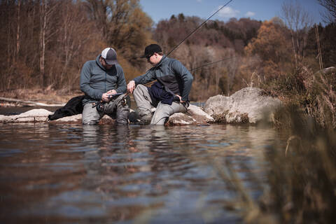 Fischer sitzt mit Sohn am Flussufer im Wald, lizenzfreies Stockfoto