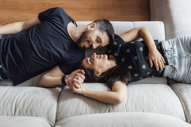 Couple relaxing while lying down on sofa at home - SASF00064