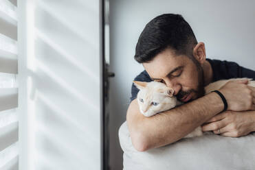 Mid adult man embracing cat in arms while sitting at home - SASF00068