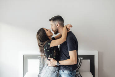 Romantisches Paar, das sich umarmt, während es auf dem Bett zu Hause kniet - SASF00074