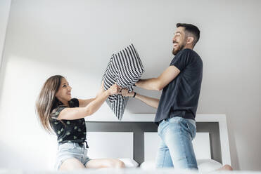 Happy couple having pillow fight on bed in bedroom - SASF00077