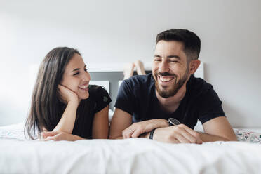 Romantisches lächelndes Paar, das im Schlafzimmer zu Hause auf der Vorderseite liegt - SASF00079