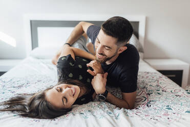 Lächelndes Paar spielt auf dem Bett im Schlafzimmer zu Hause - SASF00080
