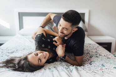 Smiling couple playing on bed in bedroom at home - SASF00080