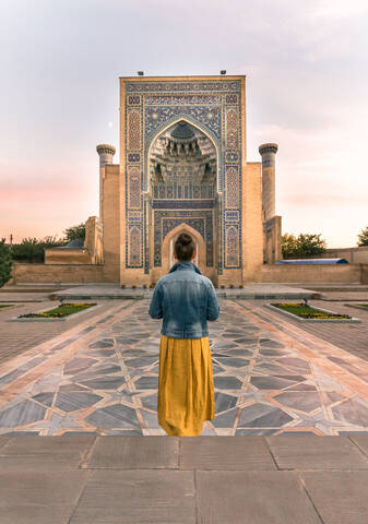 Back view of unrecognizable woman standing in doorway of shabby ornamental building in Samarkand, Uzbekistan stock photo